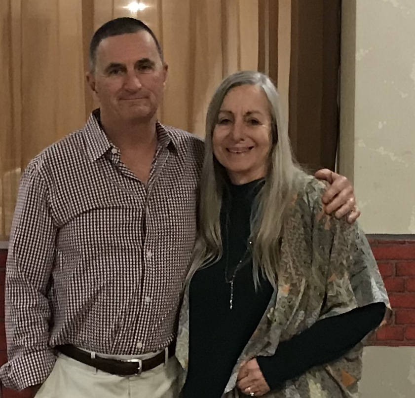 Mike and Marietta, Weststar Chimney owners. She has long blonde hair and he has short dark hair. They are dressed semi-formal standing in front of a CS emblem.